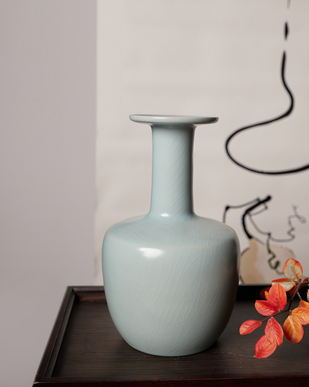 Celadon vase styled on a dark console table with red leaves and abstract wall art.