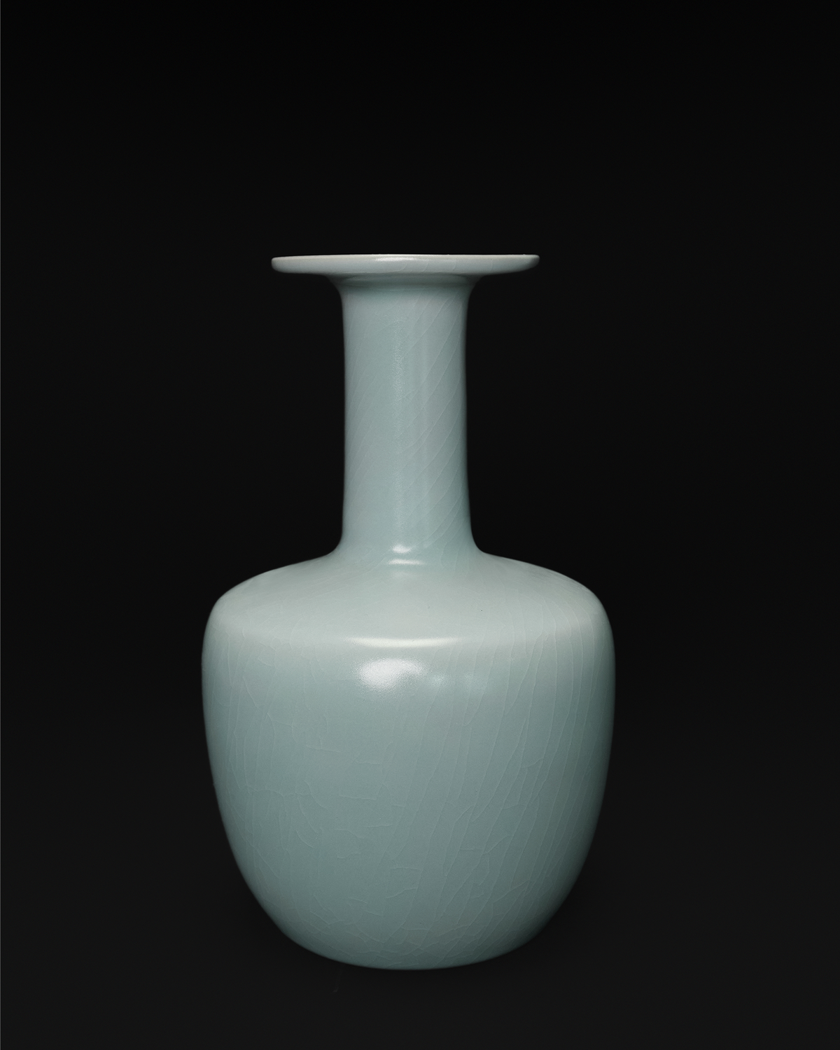 Front view of a celadon vase with a broad dish-shaped mouth, long neck and rounded rectangular body.