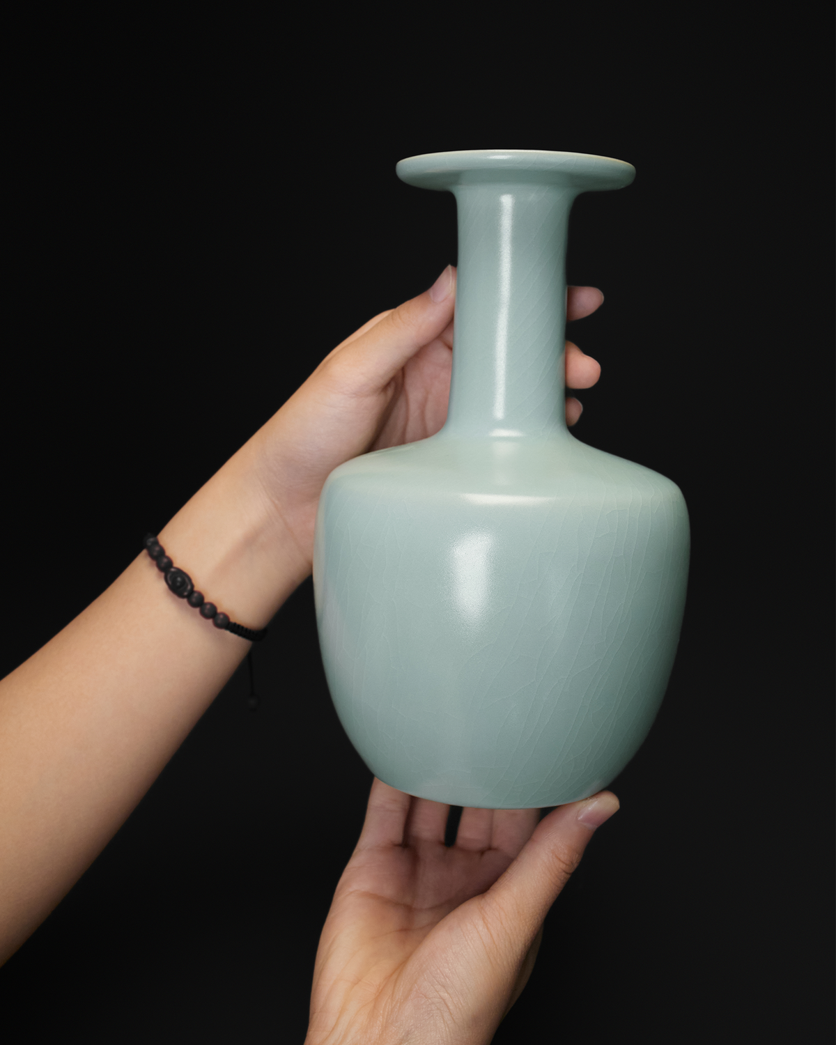 Handheld view of the celadon vase showing its scale, long neck and broad dish-shaped mouth.