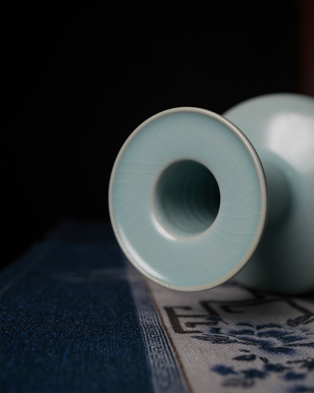 Close-up of the celadon vase dish mouth resting against a blue patterned textile.