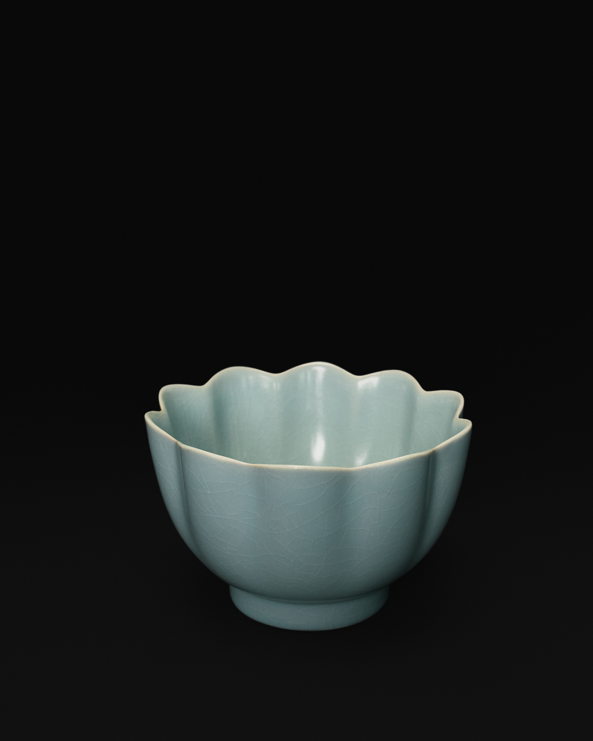 Three-quarter view of a Chinese celadon bowl with lotus-petal sides and a scalloped rim.
