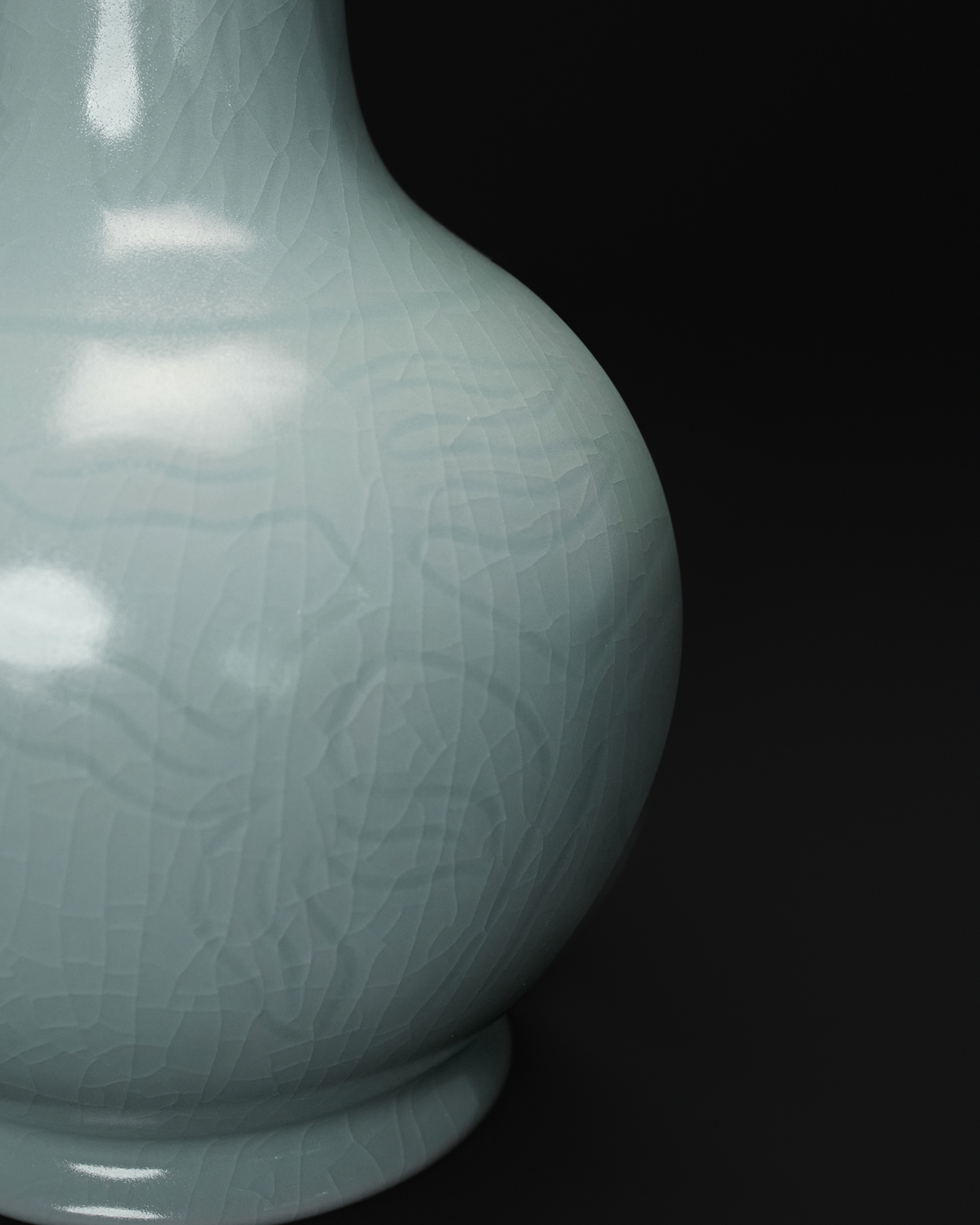 Close-up of the carved floral pattern and crackle glaze on the rounded celadon vase body.