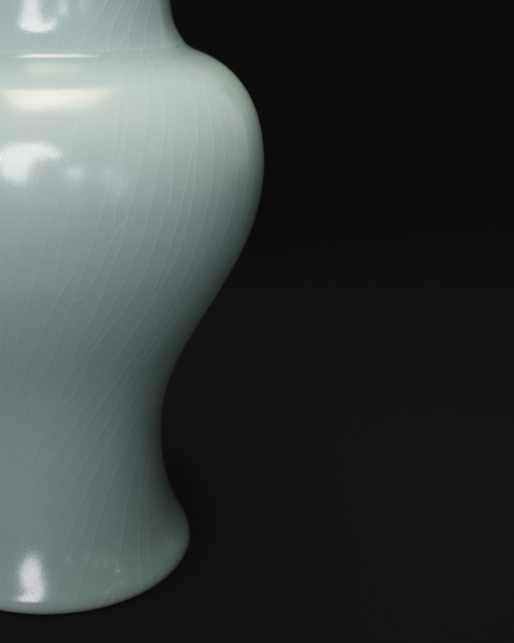 Close-up of the fine crackle glaze across the curved lower body of a celadon Guanyin vase.