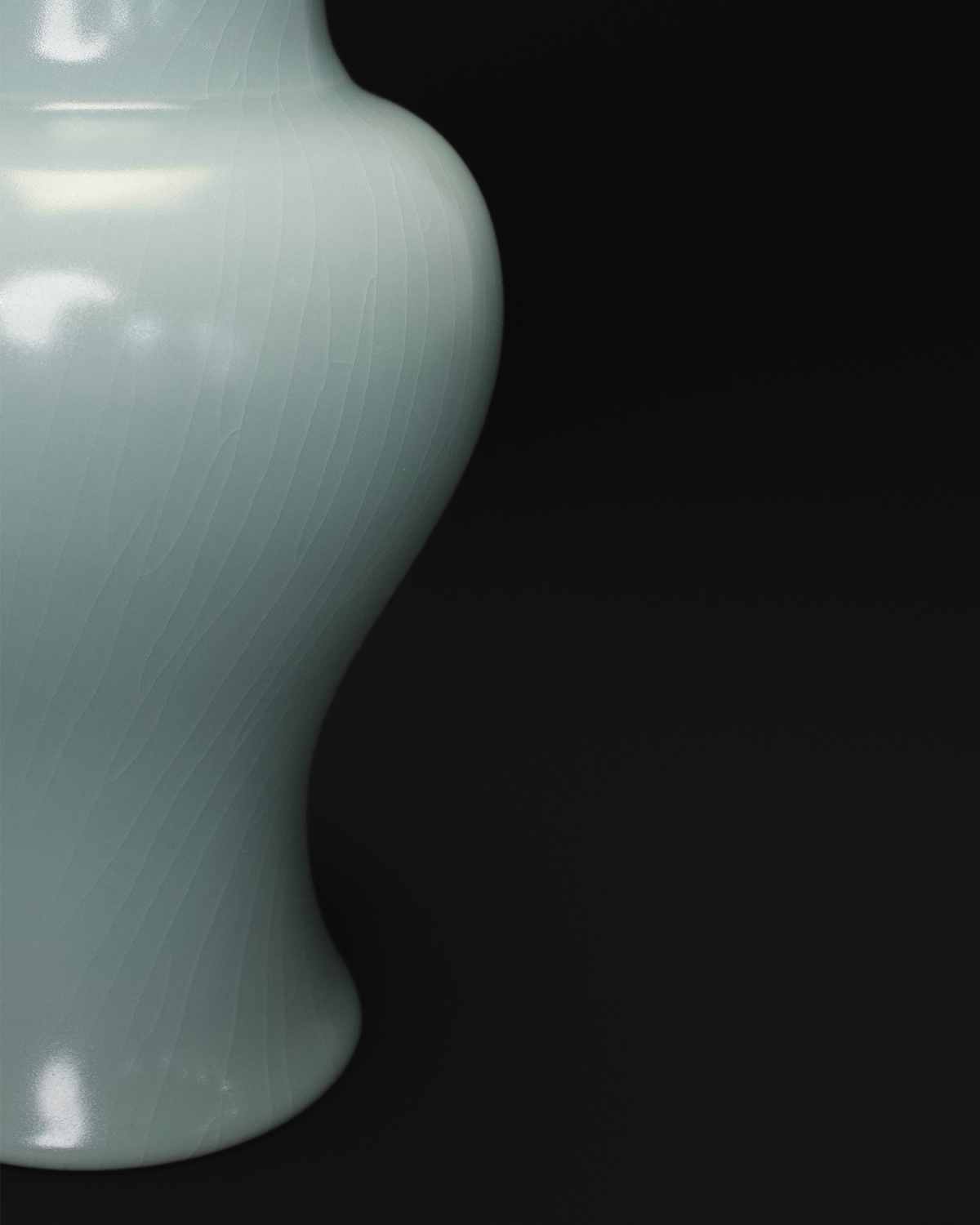 Close-up of the fine crackle glaze across the curved lower body of a celadon Guanyin vase.
