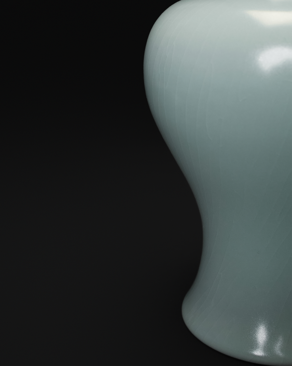 Close-up of the curved lower profile and pale celadon glaze on a Guanyin vase.