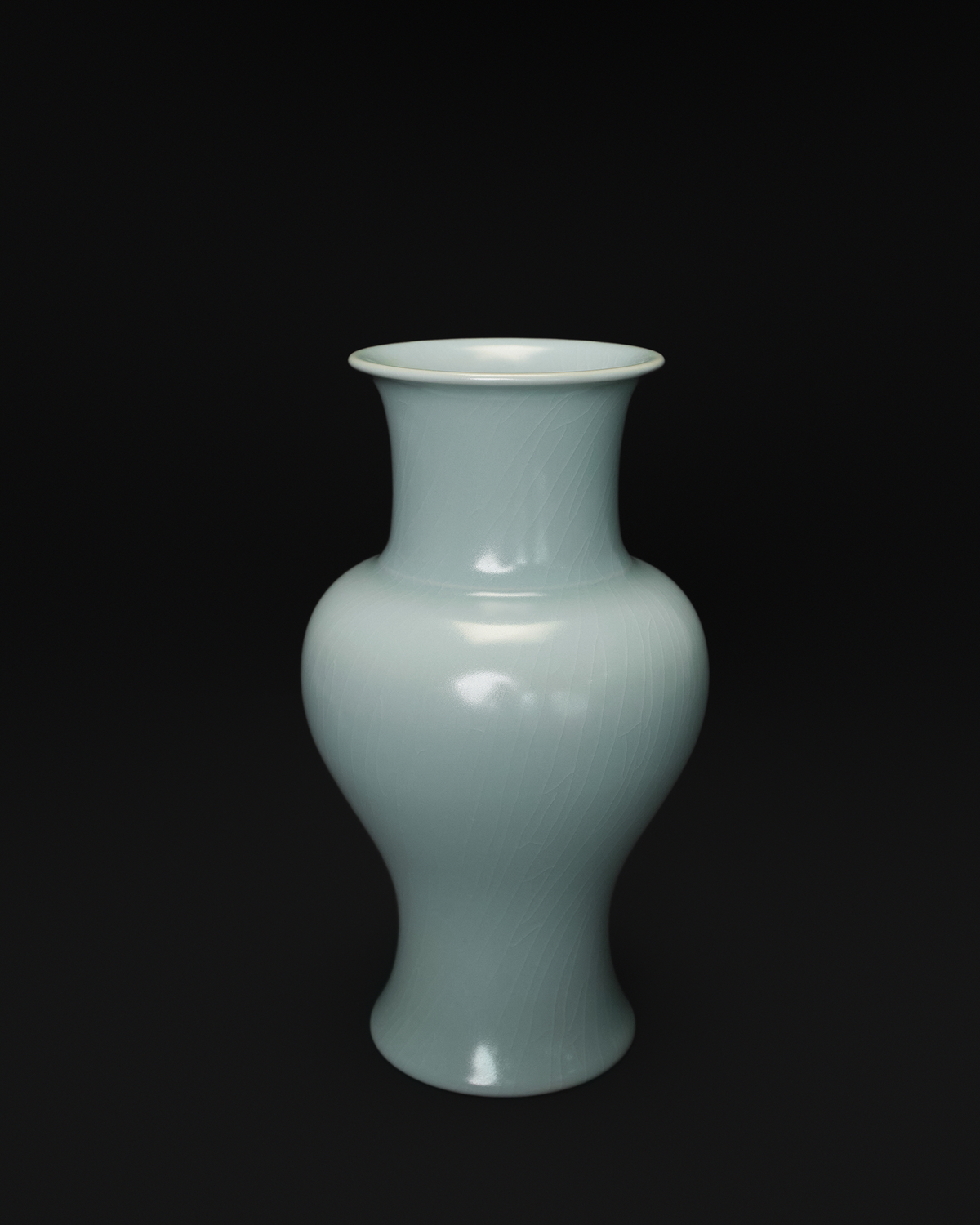 Front view of a celadon Guanyin vase with a flared rim, rounded shoulders and a waisted body.