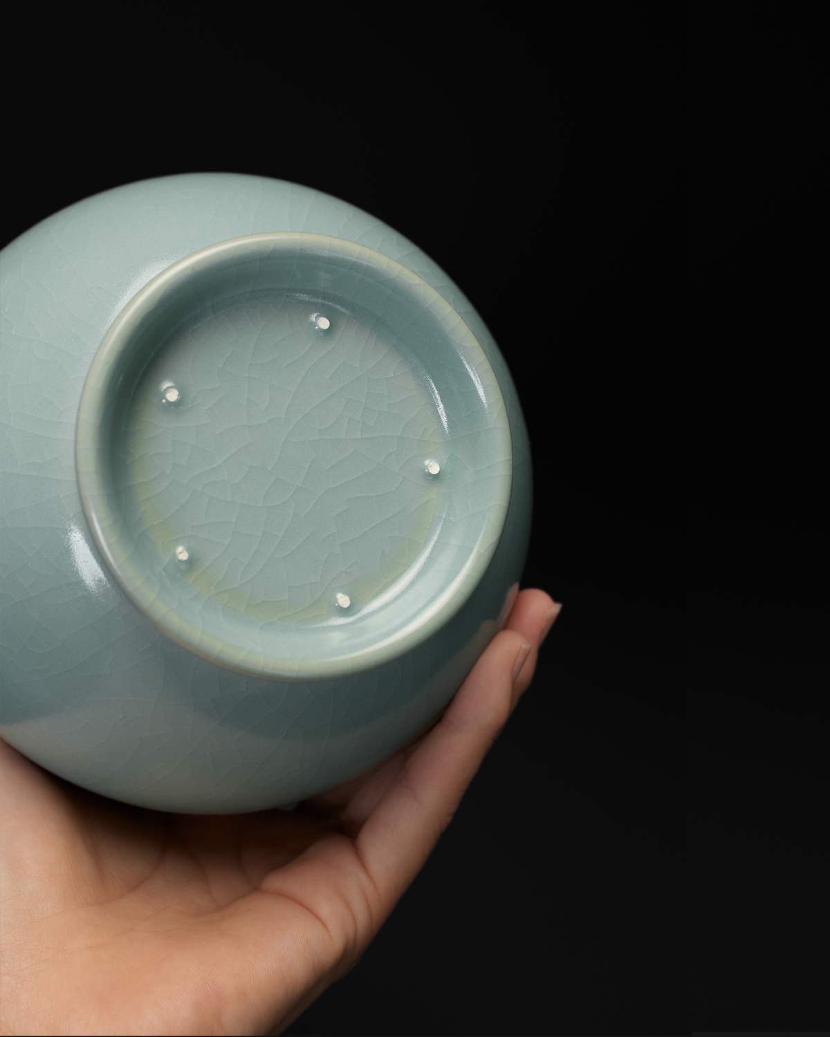 Handheld base view of the long neck vase showing fine crackle and five visible spur marks.