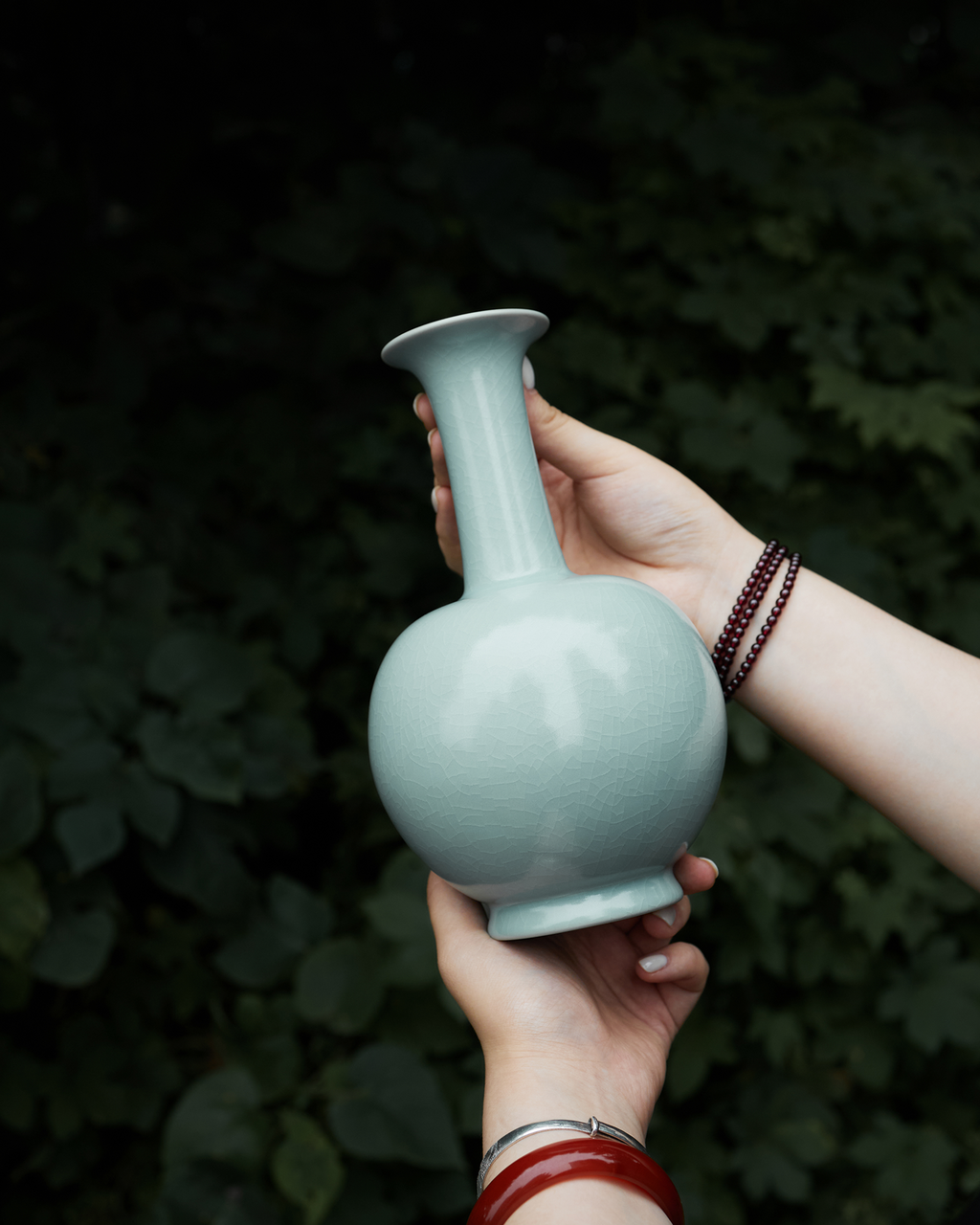 Handheld outdoor view of the celadon long neck vase against a softly blurred green background.