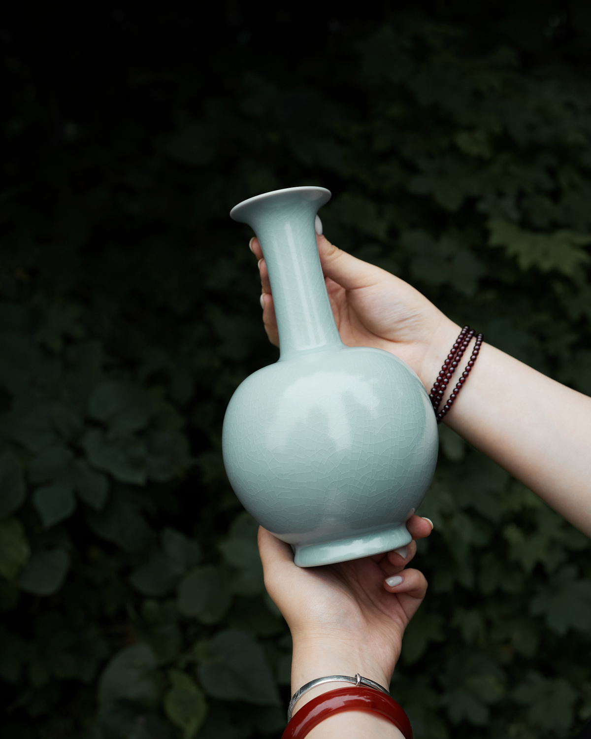 Handheld outdoor view of the celadon long neck vase against a softly blurred green background.