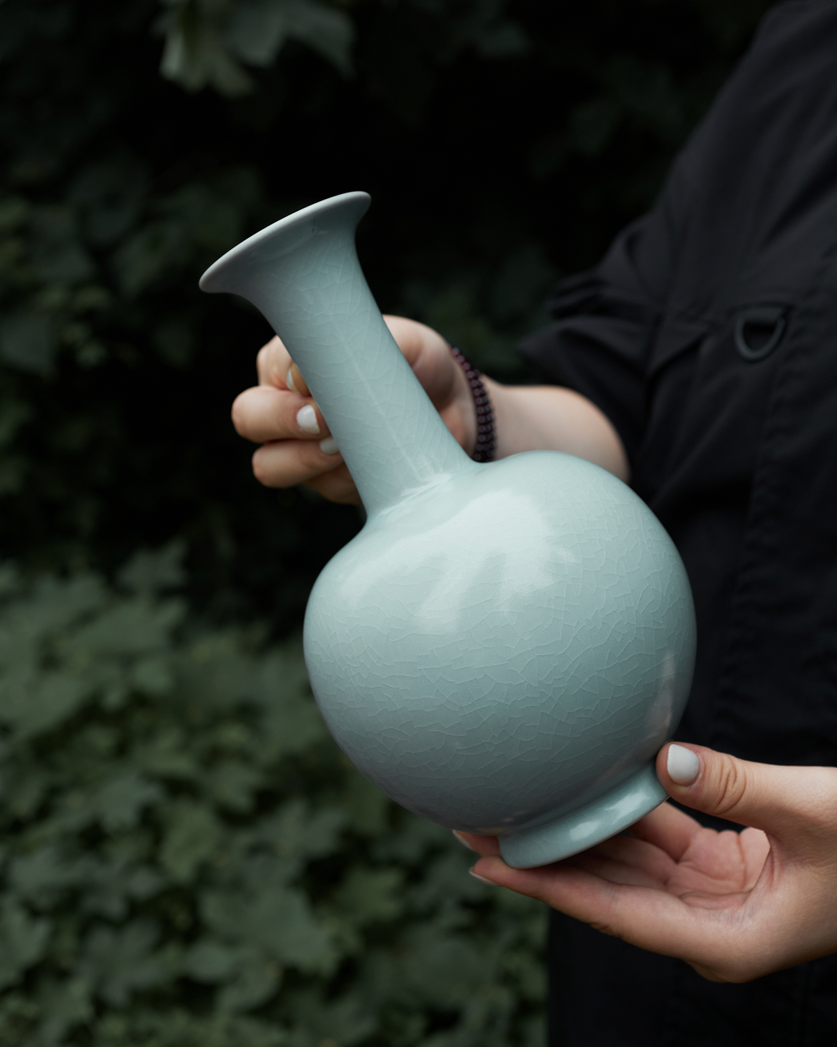 Angled handheld view of the long neck vase outdoors, showing its scale and rounded silhouette.