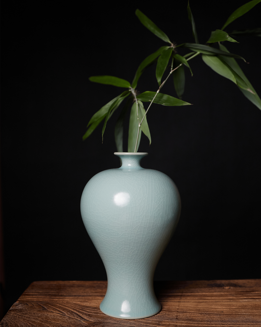 Celadon Meiping vase holding leafy branches as a sculptural accent on a wooden table.