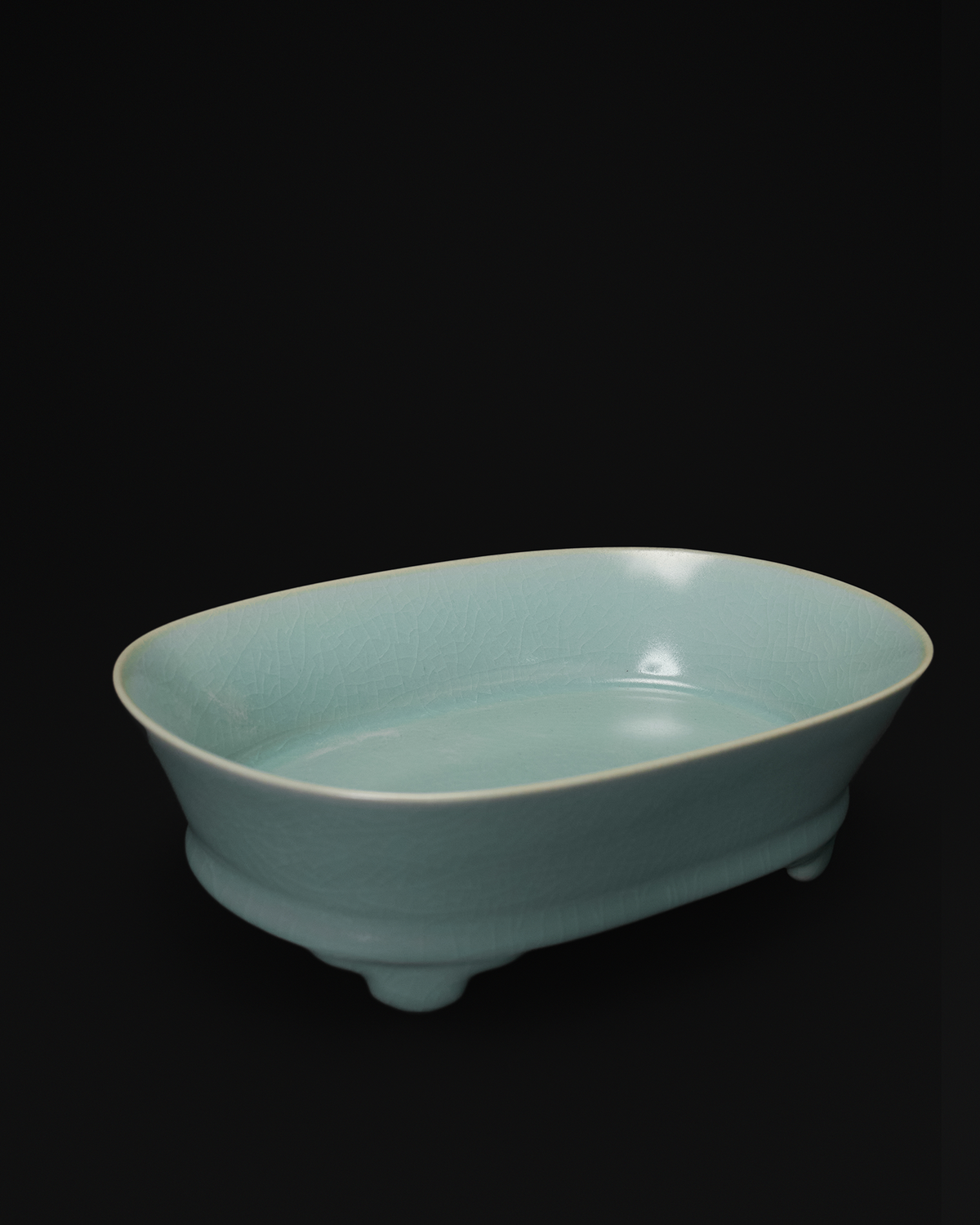 Angled view of a celadon narcissus basin with a softly flared rim and raised feet.