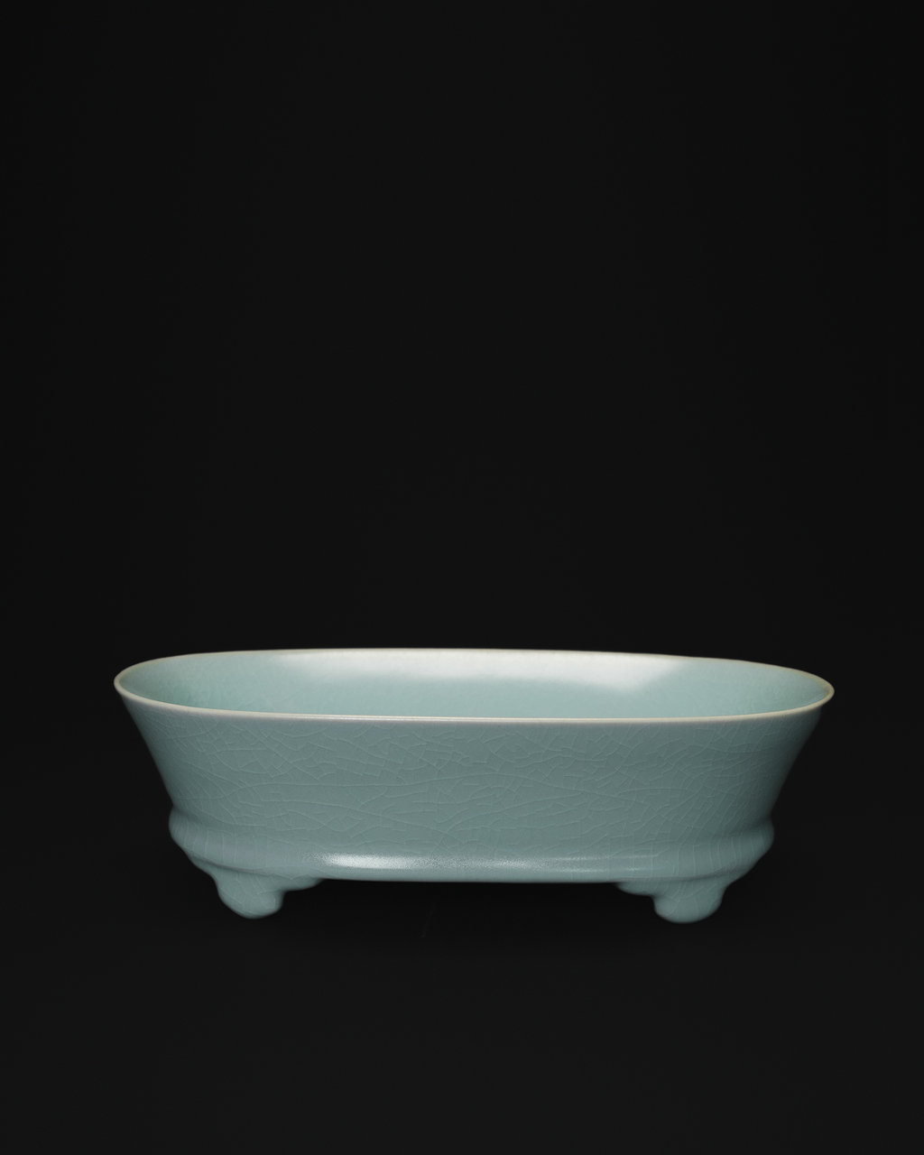 Front view of a celadon narcissus basin with an oval body and raised feet on a black background.