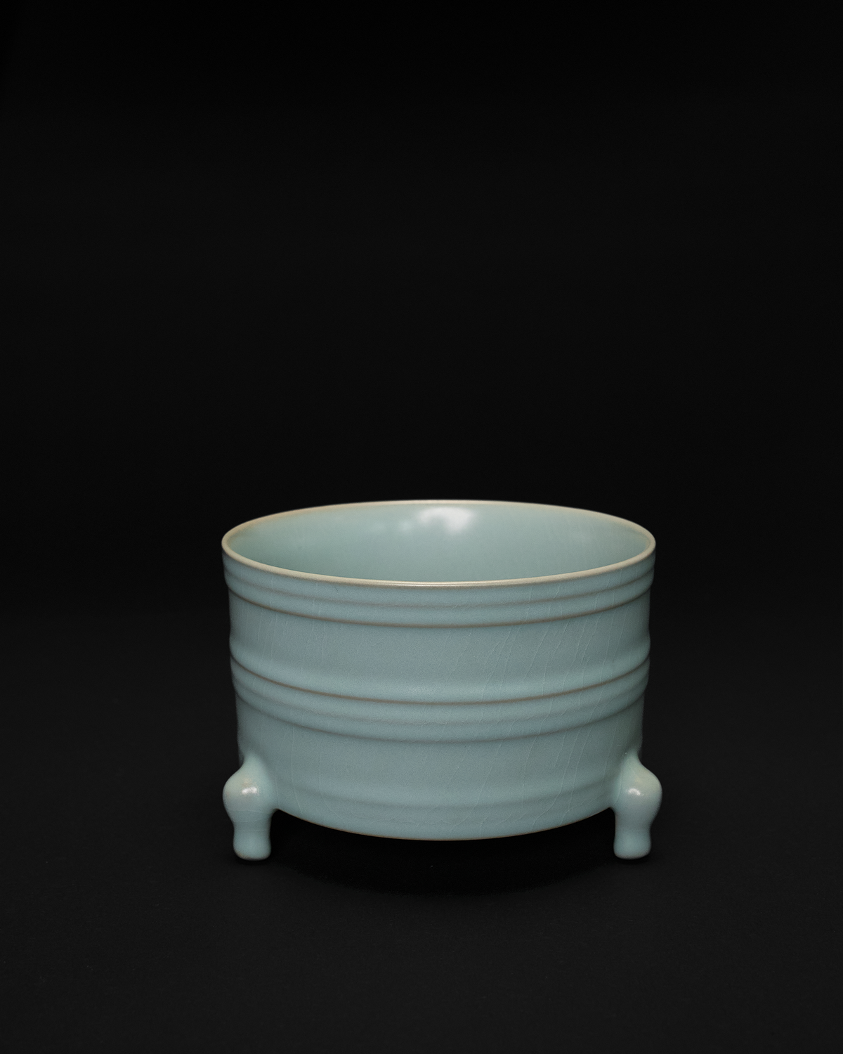 Front view of a ribbed ceramic vase with horizontal bowstring bands and three sculpted feet.