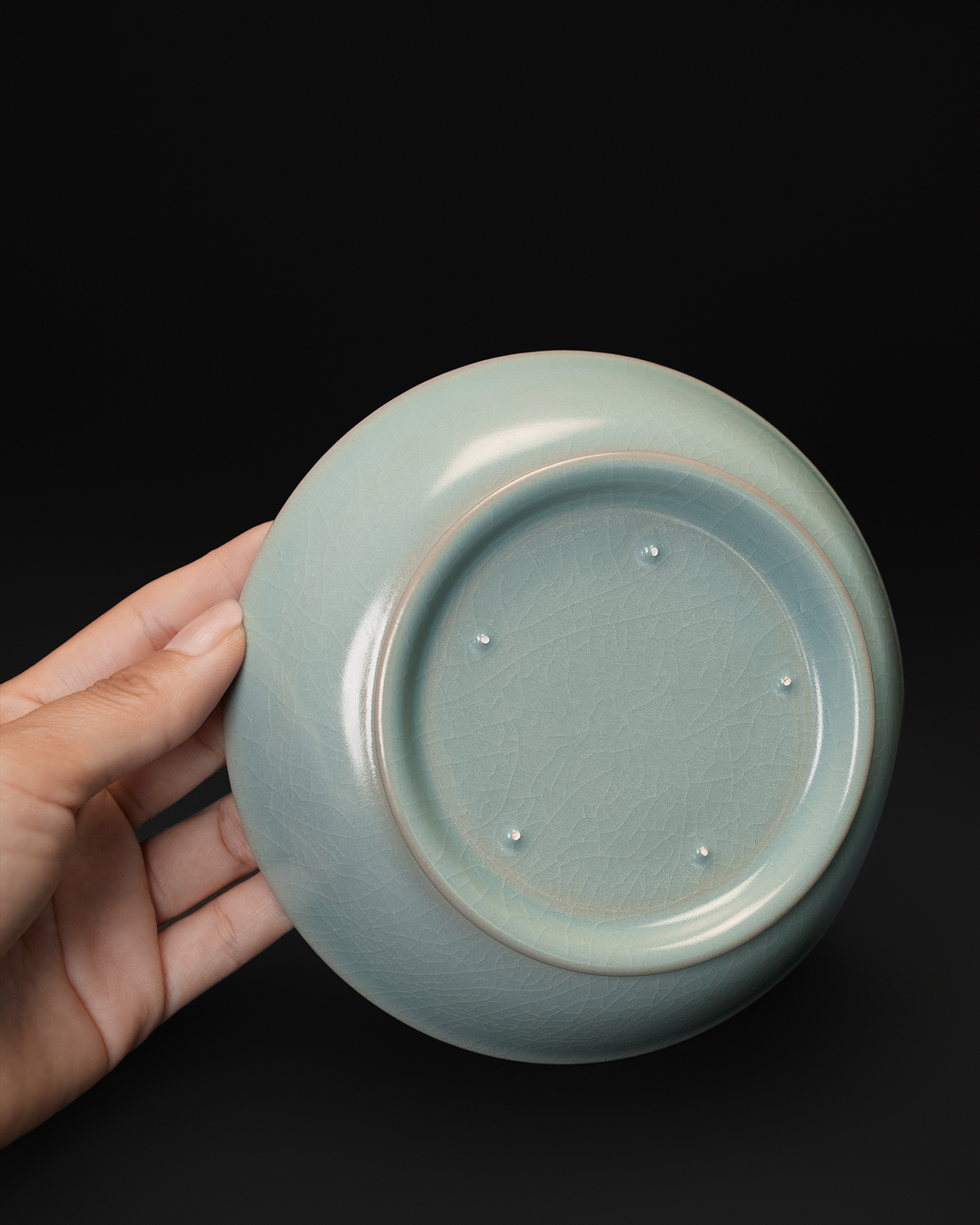 Handheld underside view of the Ru ware brush washer showing its foot ring and five spur marks.