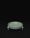 Three-quarter view of the celadon tripod bowl showing its shallow interior and three feet.