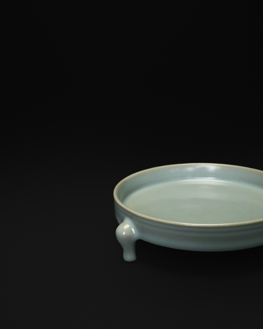 Close-up of one sculpted foot and the shallow rim profile of the celadon tripod bowl.
