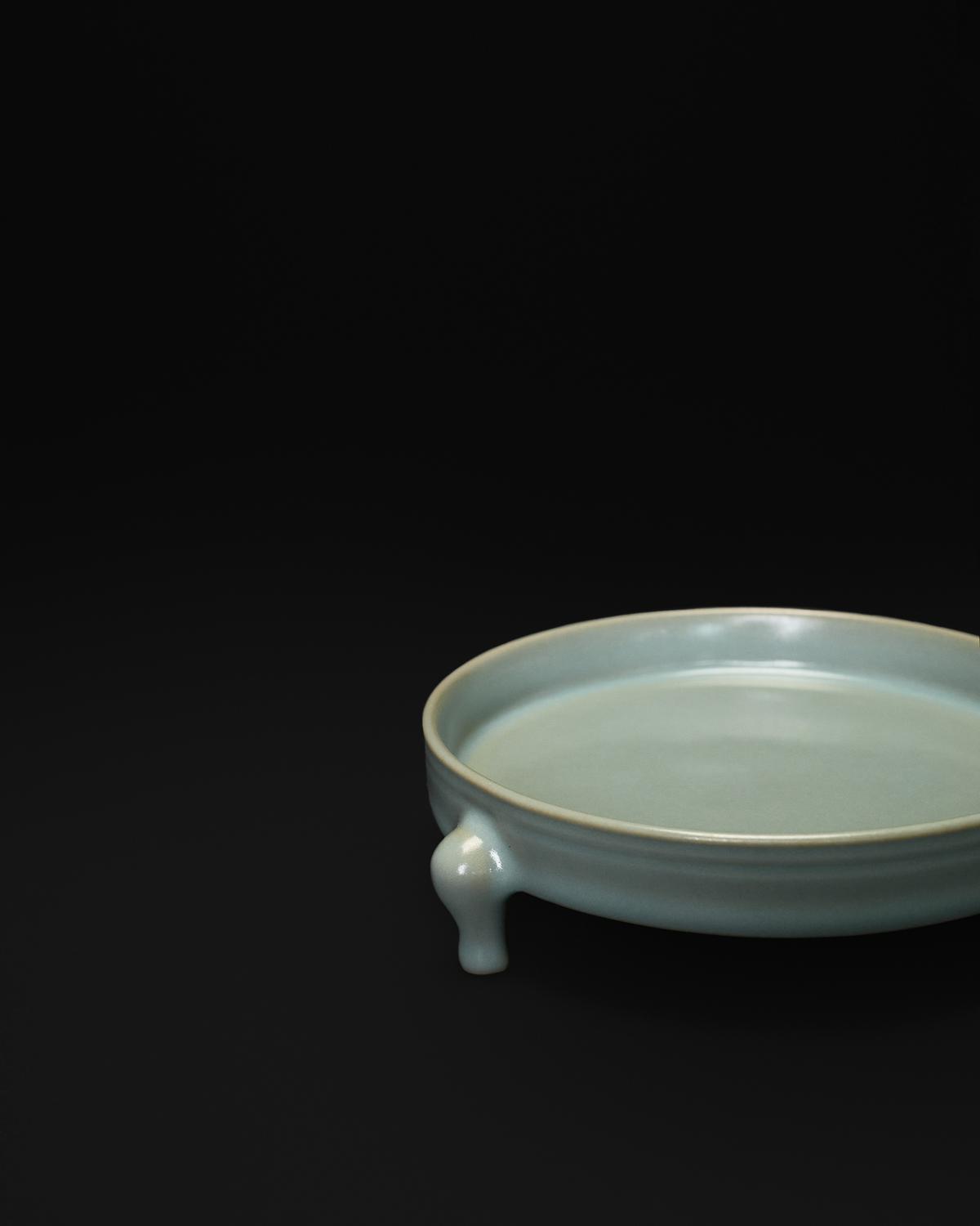 Close-up of one sculpted foot and the shallow rim profile of the celadon tripod bowl.
