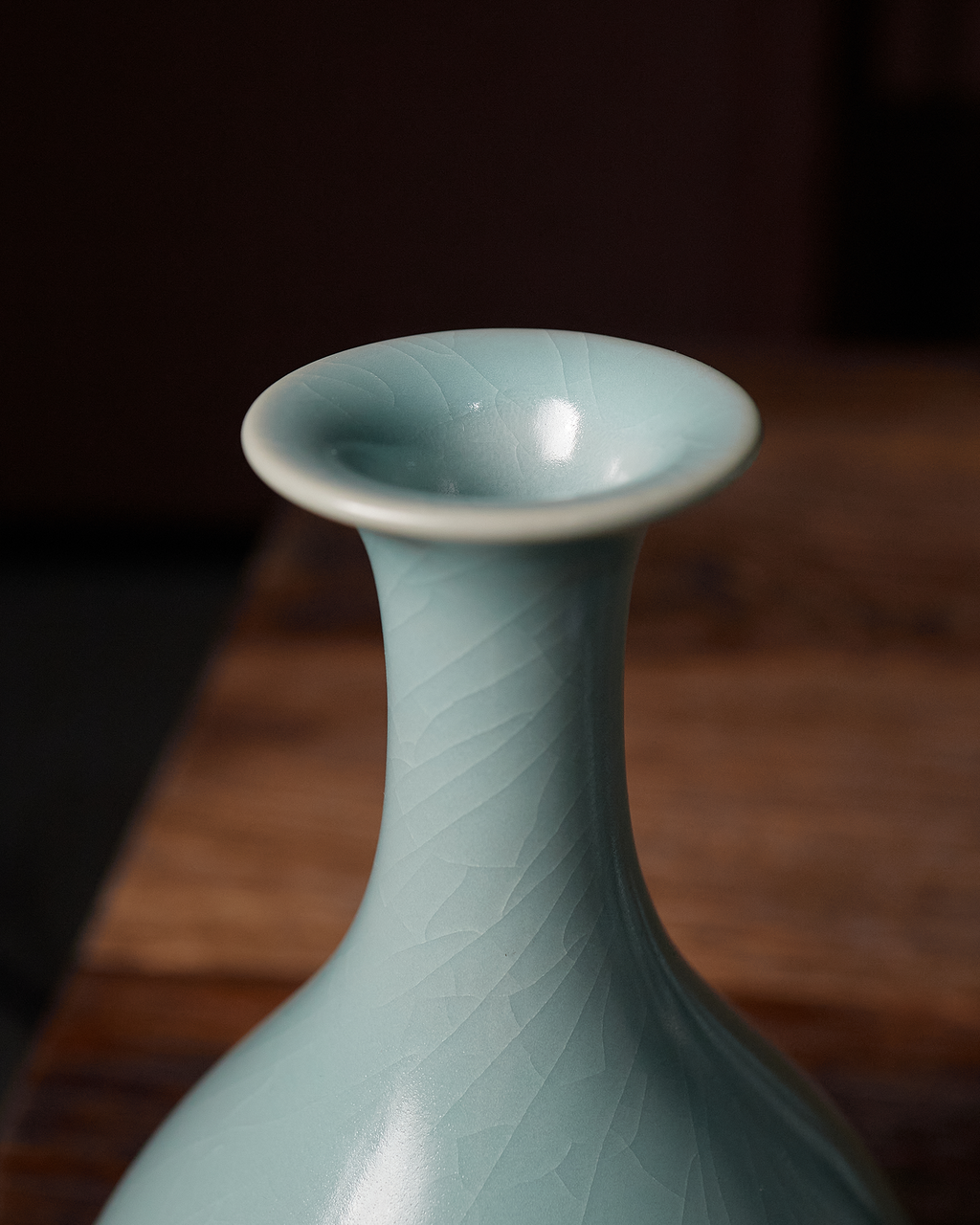 Close-up of the flared rim and slender neck of a Yuhuchun vase on a wooden table.