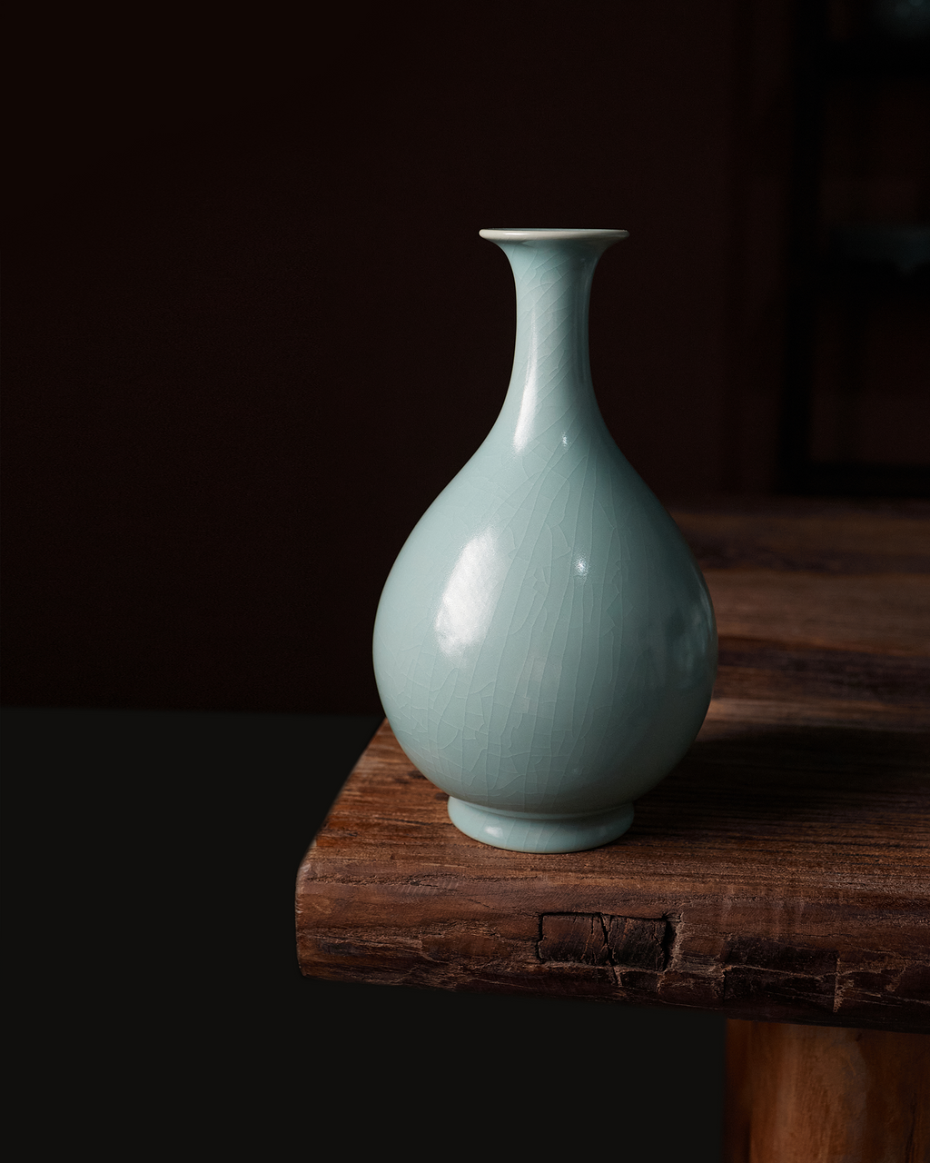 Celadon Yuhuchun vase displayed on a rustic wooden table in a softly lit interior.